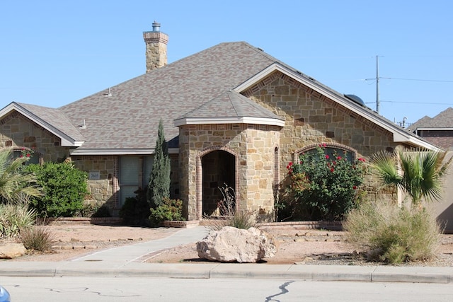 view of front of home featuring stone siding, a chimney, and a shingled roof