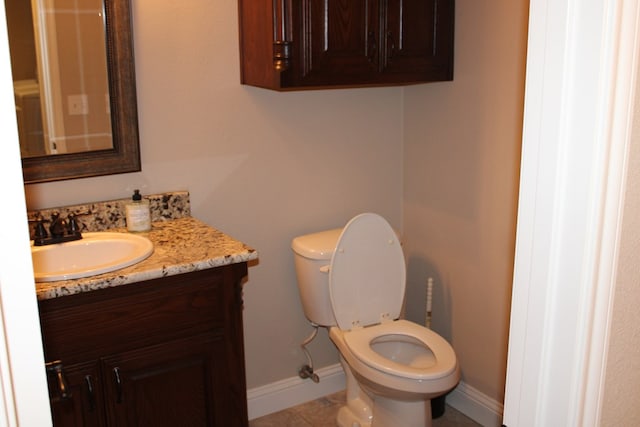 half bathroom with baseboards, vanity, and toilet