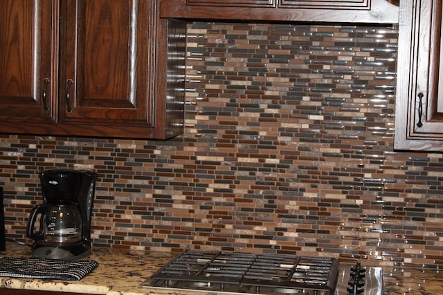 kitchen view of backsplash, dark brown cabinetry, and stainless steel gas cooktop