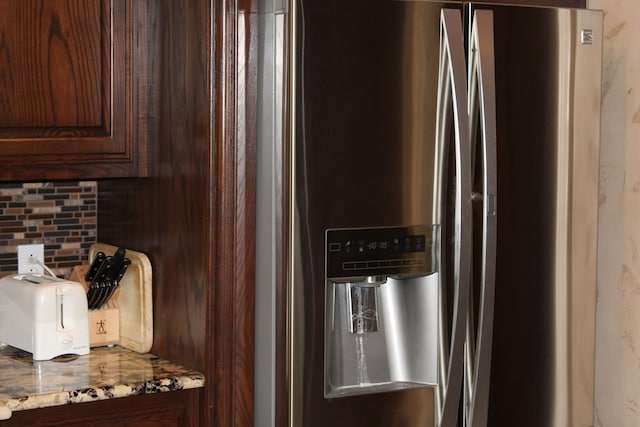 kitchen view of stainless steel fridge with ice dispenser, decorative backsplash, light stone countertops, and dark brown cabinetry