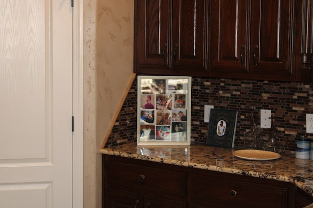 kitchen featuring wallpapered walls, tasteful backsplash, dark brown cabinets, and light stone counters