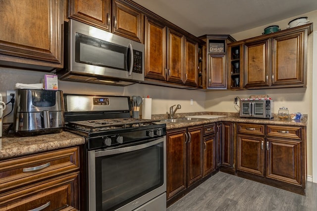 kitchen featuring sink, appliances with stainless steel finishes, dark stone counters, dark brown cabinetry, and dark wood-type flooring