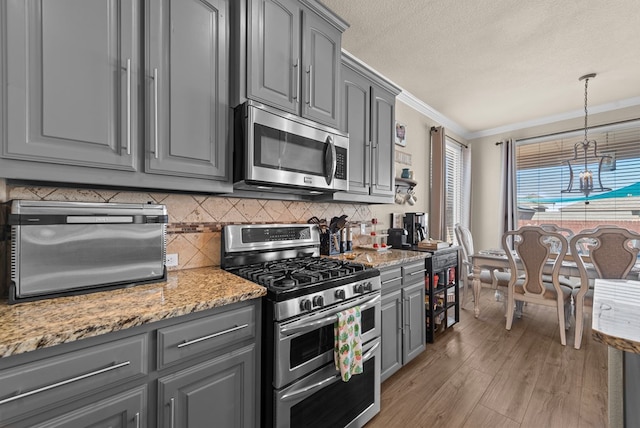7028 Xit Ranch Rd, Odessa, TX 79765 - kitchen featuring stainless steel appliances, gray cabinetry, light wood-type flooring, backsplash, and crown molding