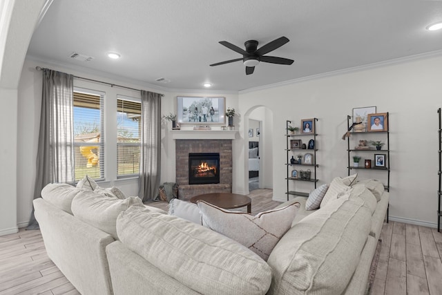living area featuring ornamental molding, a fireplace, ceiling fan, light wood finished floors, and arched walkways