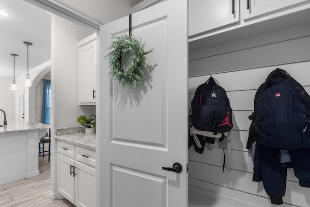 interior space with light stone counters, pendant lighting, light wood-style flooring, white cabinetry, and arched walkways