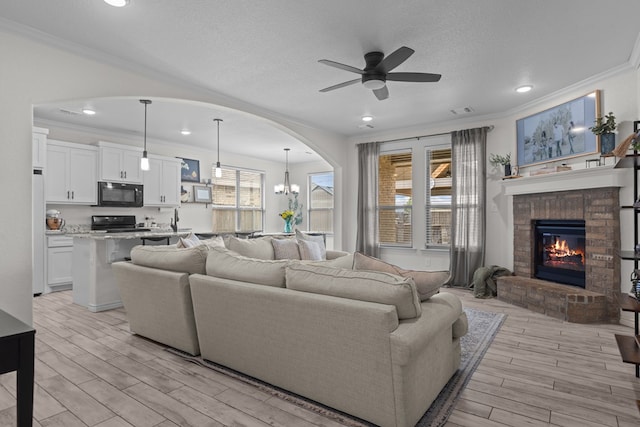 living area with light wood-style flooring, recessed lighting, ornamental molding, ceiling fan with notable chandelier, and a fireplace