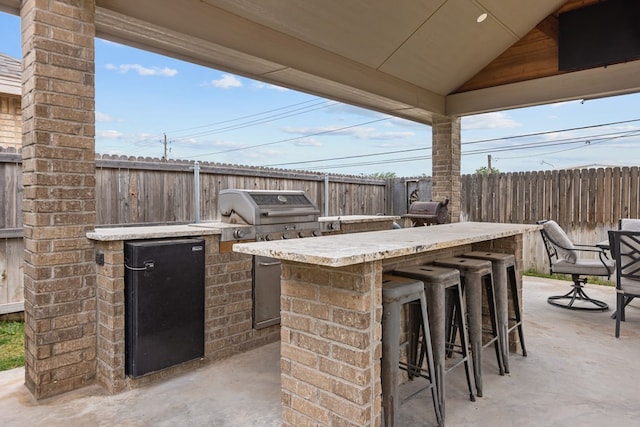 view of patio with fence, area for grilling, an outdoor kitchen, and outdoor wet bar