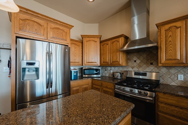 kitchen with wall chimney exhaust hood, backsplash, dark stone counters, and appliances with stainless steel finishes