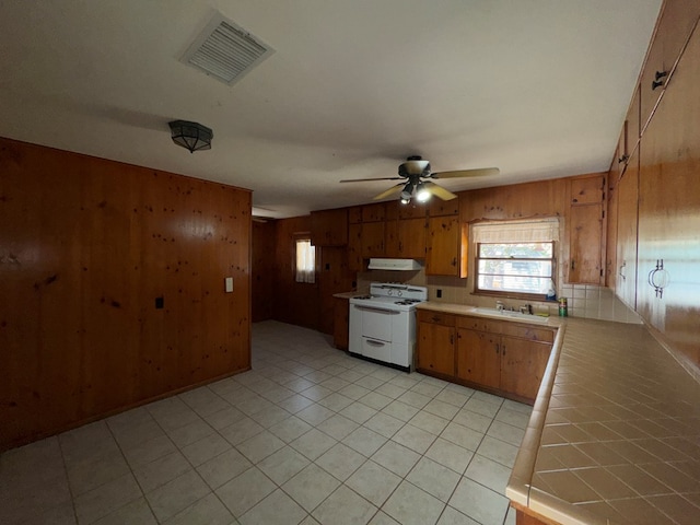 kitchen with wooden walls, a sink, tile counters, white gas range, and visible vents