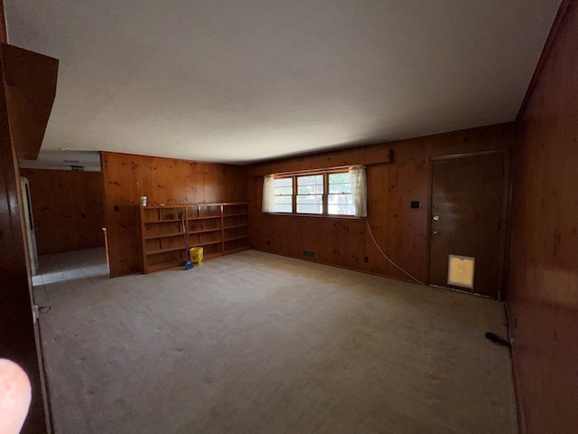 unfurnished living room featuring visible vents, wood walls, and light carpet
