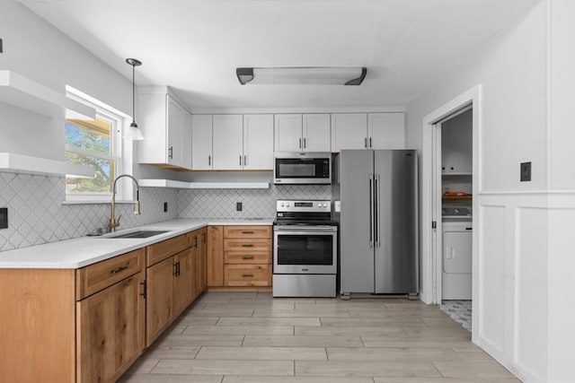 kitchen with stainless steel appliances, a sink, washer / dryer, and white cabinets