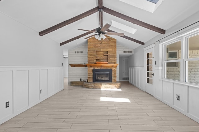unfurnished living room with a skylight, a large fireplace, light wood finished floors, a decorative wall, and a ceiling fan