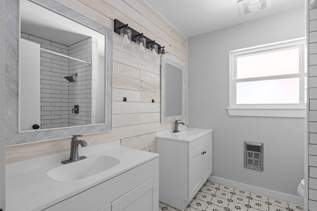 bathroom featuring two vanities, heating unit, a tile shower, wooden walls, and baseboards