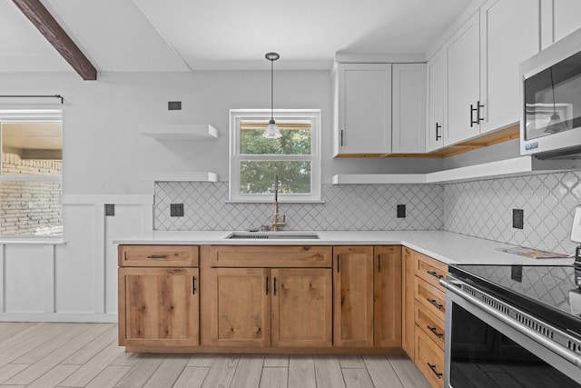 kitchen featuring stainless steel appliances, a sink, light countertops, light wood-style flooring, and backsplash