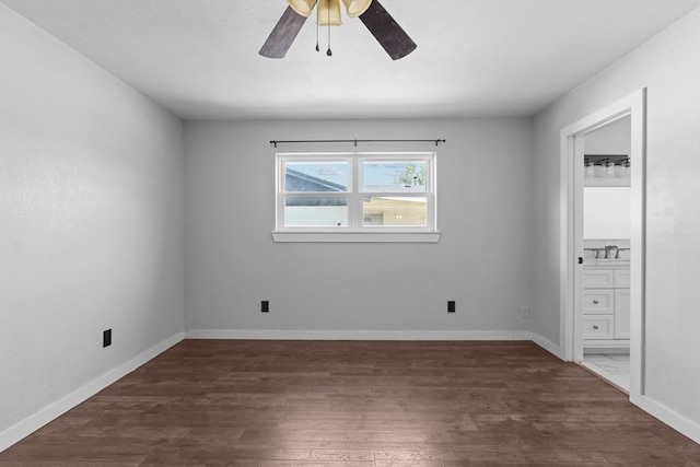 unfurnished bedroom with dark wood-style flooring, connected bathroom, baseboards, a sink, and a ceiling fan