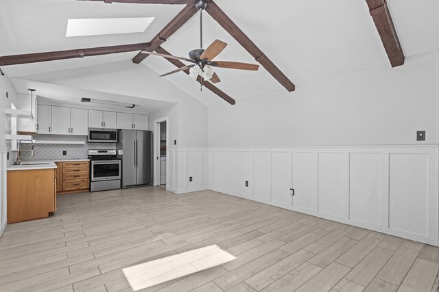 kitchen featuring stainless steel appliances, light countertops, a skylight, wainscoting, and ceiling fan