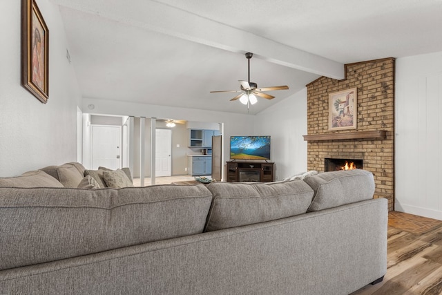 living room with vaulted ceiling with beams, light hardwood / wood-style floors, a brick fireplace, and ceiling fan