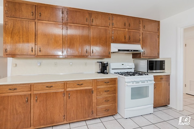 kitchen with under cabinet range hood, light tile patterned floors, stainless steel microwave, light countertops, and white range with gas cooktop