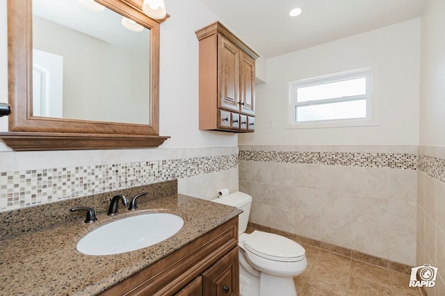 bathroom with toilet, tile walls, vanity, and a wainscoted wall