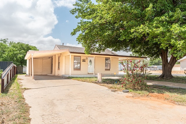 view of front of house with fence, a carport, roof with shingles, brick siding, and driveway