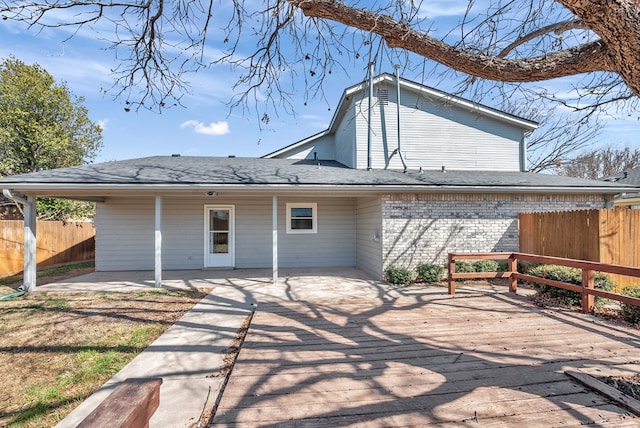 rear view of property with brick siding, roof with shingles, a patio area, and fence