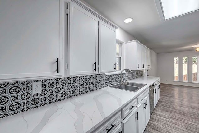 kitchen featuring light stone counters, a sink, white cabinetry, and decorative backsplash