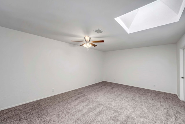 carpeted empty room featuring ceiling fan, a skylight, visible vents, and baseboards