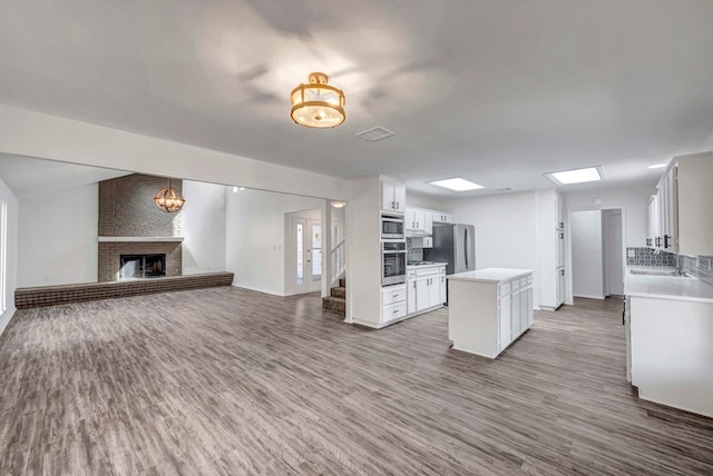 kitchen with white cabinets, open floor plan, stainless steel appliances, light countertops, and a fireplace