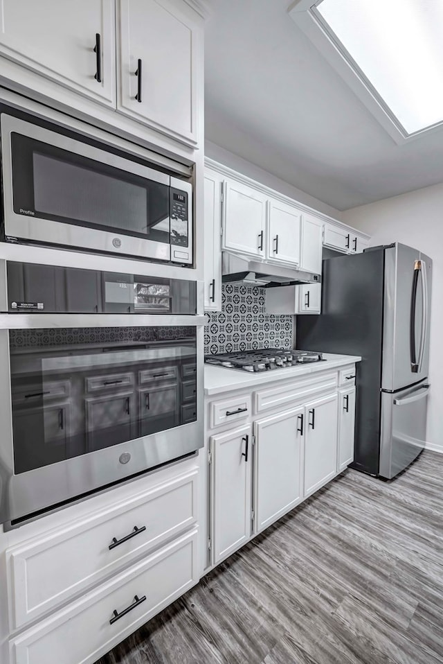 kitchen with under cabinet range hood, tasteful backsplash, white cabinetry, and stainless steel appliances