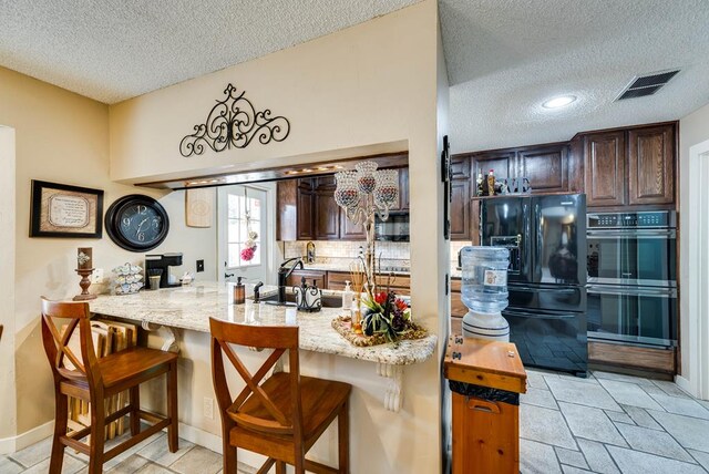 2919 Kirkwood Dr, Odessa, TX 79762 - kitchen with black refrigerator with ice dispenser, double oven, a textured ceiling, dark brown cabinets, and a peninsula