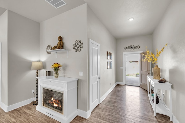 entryway featuring baseboards, a multi sided fireplace, visible vents, and wood finished floors