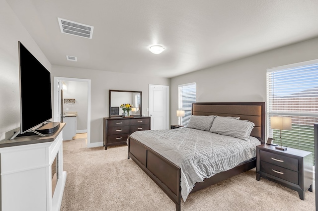 bedroom featuring ensuite bathroom, visible vents, baseboards, and light carpet
