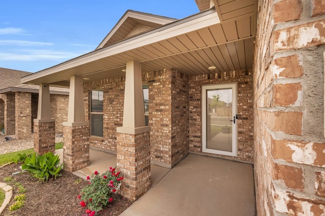 doorway to property featuring brick siding and covered porch