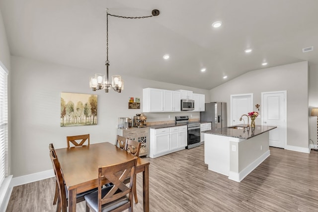 kitchen featuring a sink, a center island with sink, vaulted ceiling, a notable chandelier, and appliances with stainless steel finishes