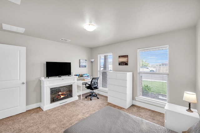 carpeted home office with visible vents, baseboards, and a lit fireplace