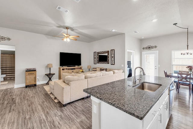 kitchen with a sink, dark stone counters, wood finished floors, visible vents, and ceiling fan