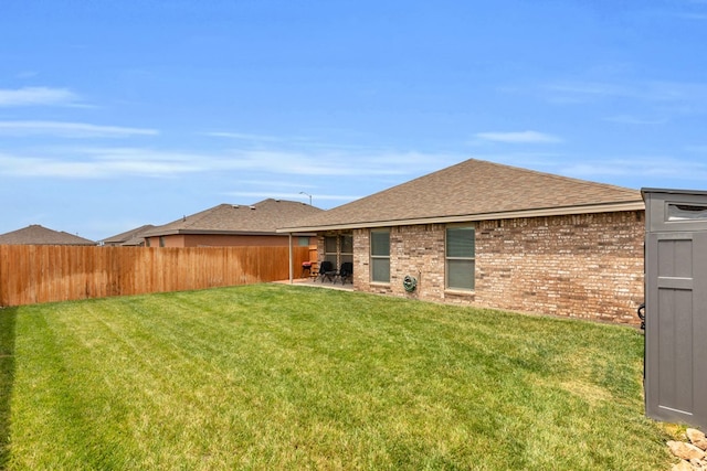 back of house featuring a yard, fence, a shingled roof, and brick siding
