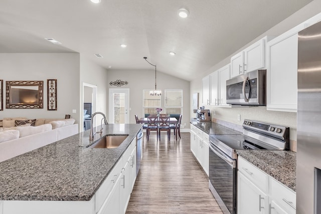 kitchen featuring a sink, vaulted ceiling, a kitchen island with sink, appliances with stainless steel finishes, and wood finished floors