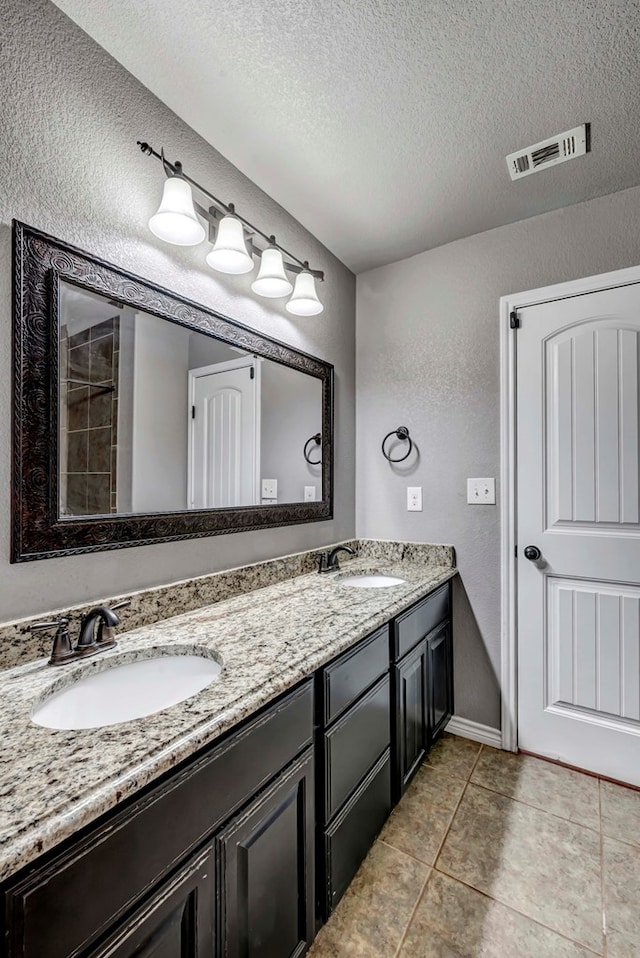 bathroom featuring double vanity, a sink, a textured ceiling, and a textured wall