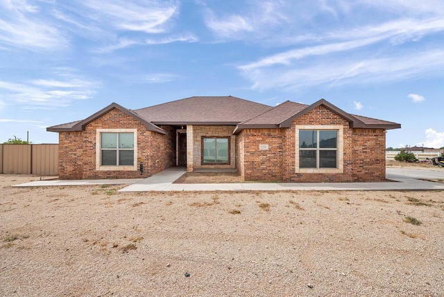 view of front of home featuring fence, roof with shingles, and brick siding