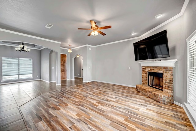 unfurnished living room featuring visible vents, arched walkways, a fireplace, wood finished floors, and ceiling fan with notable chandelier