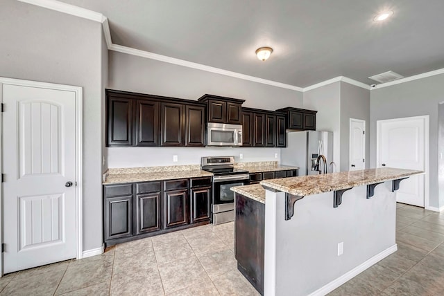 kitchen with appliances with stainless steel finishes, a breakfast bar area, a kitchen island with sink, light tile patterned floors, and ornamental molding