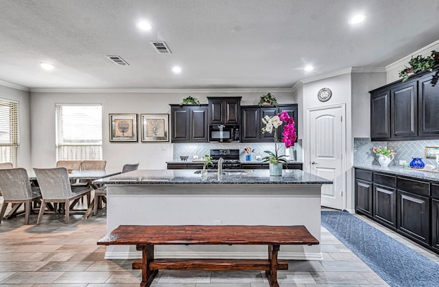 7016 Spur Ranch Rd, Odessa, TX 79765 - kitchen with black microwave, ornamental molding, a center island with sink, tasteful backsplash, and recessed lighting