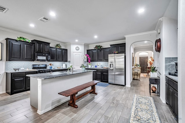 7016 Spur Ranch Rd, Odessa, TX 79765 - kitchen featuring stainless steel fridge, black microwave, gas stove, arched walkways, and decorative backsplash