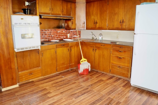 708 W Yukon Rd, Odessa, TX 79764 - kitchen with white appliances, brown cabinetry, a sink, backsplash, and light wood finished floors