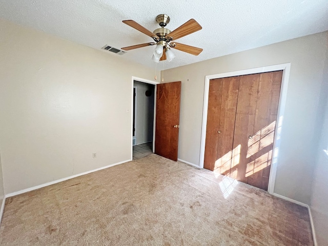 unfurnished bedroom with a textured ceiling, a closet, light colored carpet, and ceiling fan