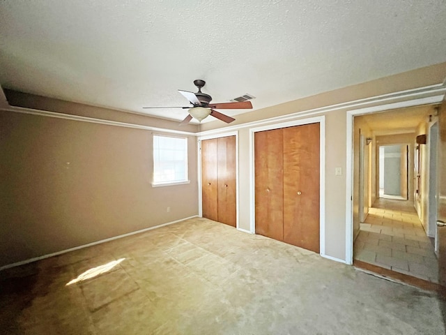 unfurnished bedroom featuring carpet flooring, multiple closets, ceiling fan, and a textured ceiling