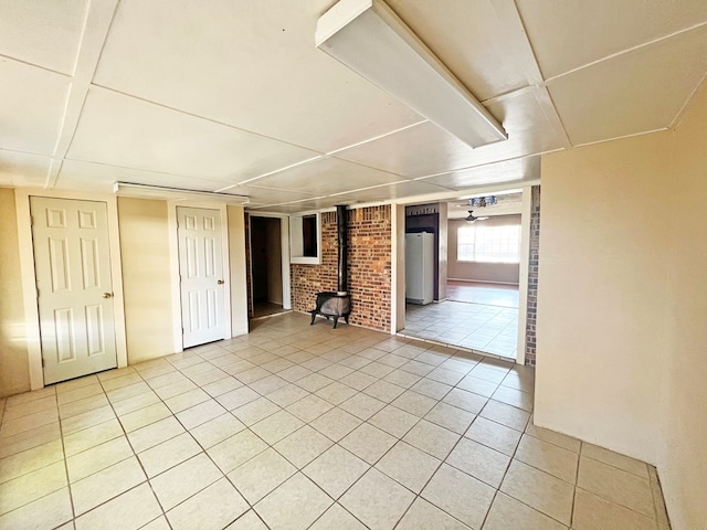 interior space featuring tile patterned flooring, white fridge, a wood stove, and brick wall