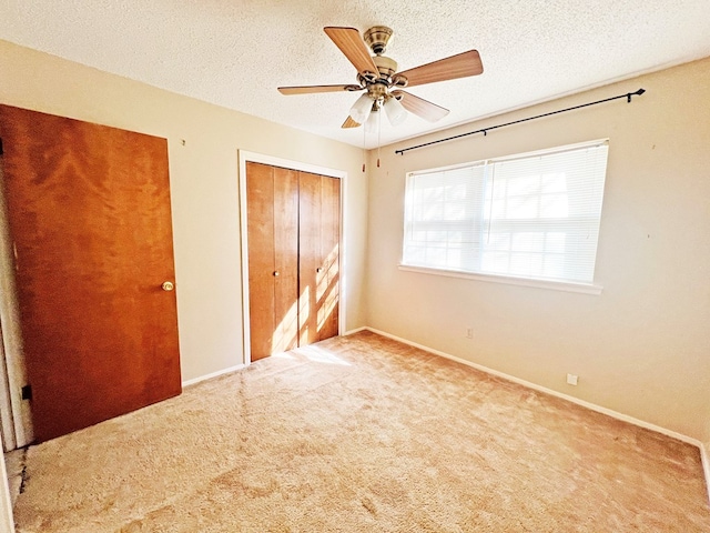 unfurnished bedroom with a textured ceiling, a closet, light colored carpet, and ceiling fan