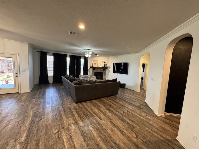 7001 La Escalera Ct, Odessa, TX 79765 - living room featuring dark wood finished floors, arched walkways, a fireplace, a textured ceiling, and ornamental molding